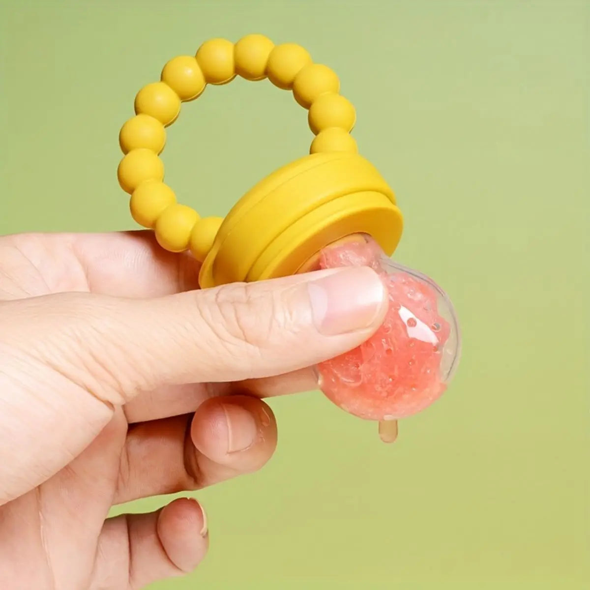 Baby's silicone fruit feeder pacifier in hand with pink fruit inside, perfect for teething and mess-free snacking.